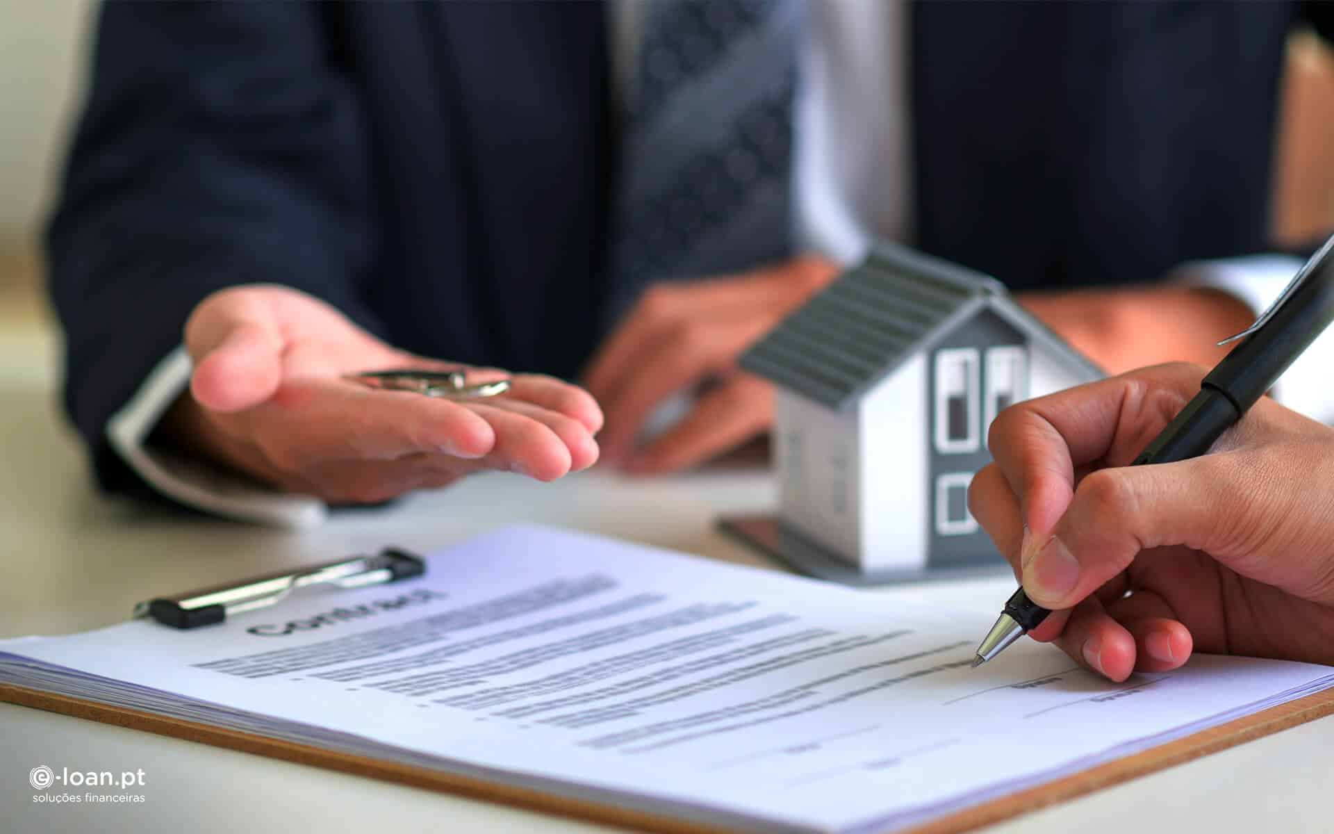 Momento de assinar o contrato imobiliário. Mão segura caneta para assinar documento da casa, com maquete de casa cinzenta. Agente estende a mão com chaves da nova casa.