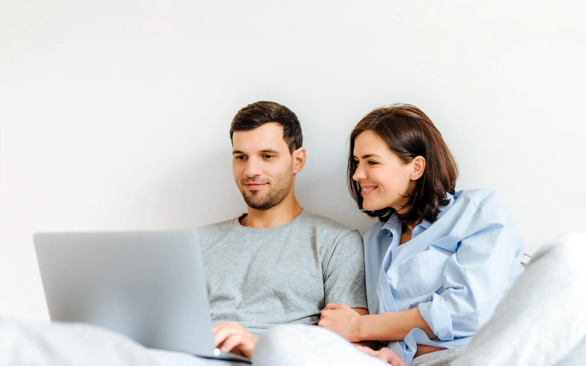 Casal jovem sorridente usa computador.